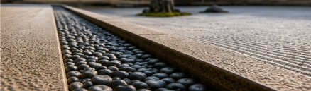 石庭の縁、黒い玉砂利と切石、向こうに砂紋