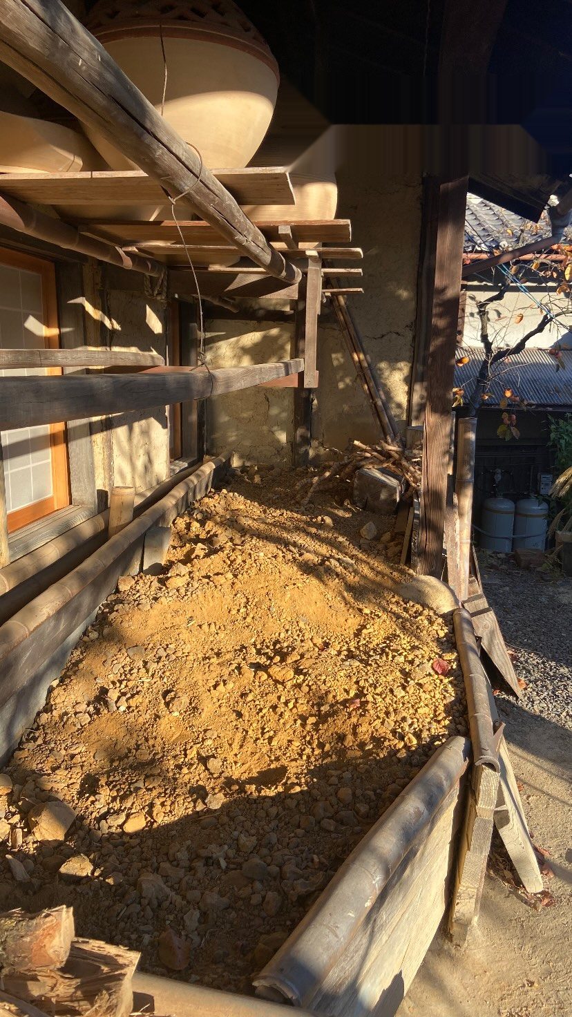 窯元の壁ぎわに干された陶土と木組みの棚、奥に大きな器