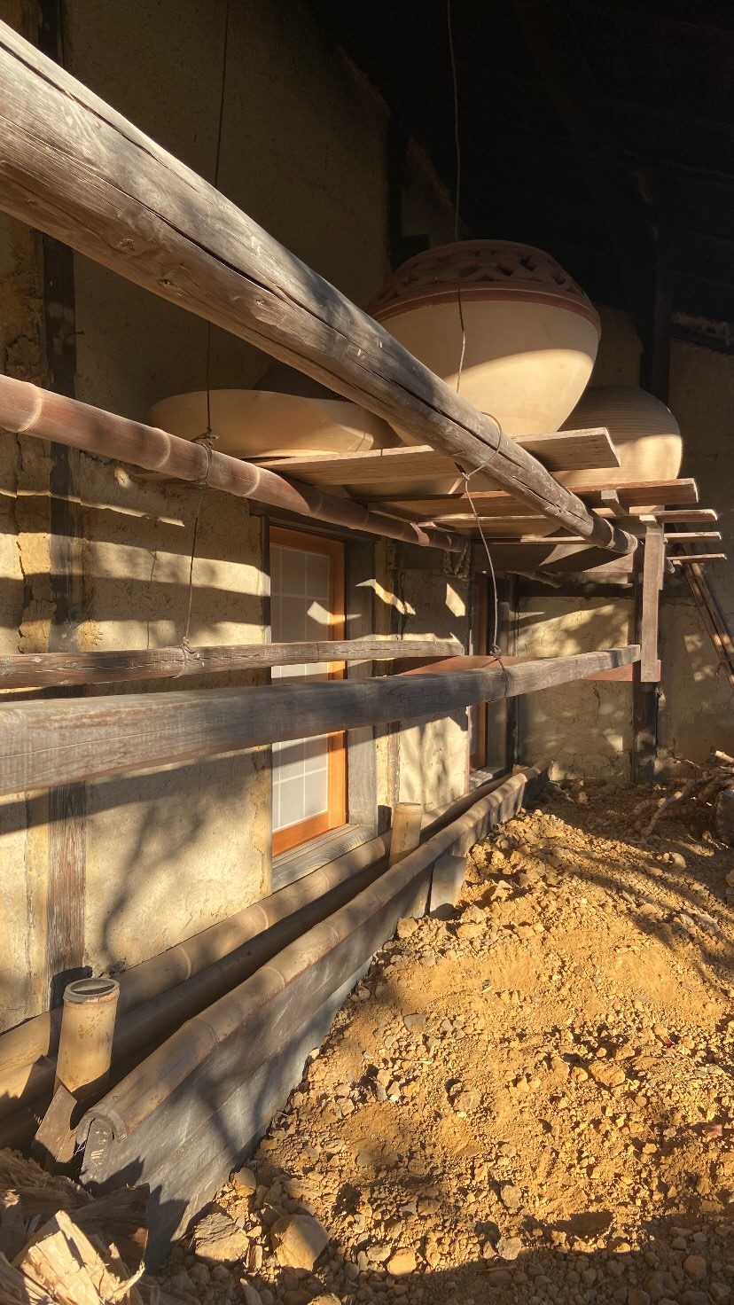 土壁の建屋ぎわに干された陶土、竹と木の棚、大きな器