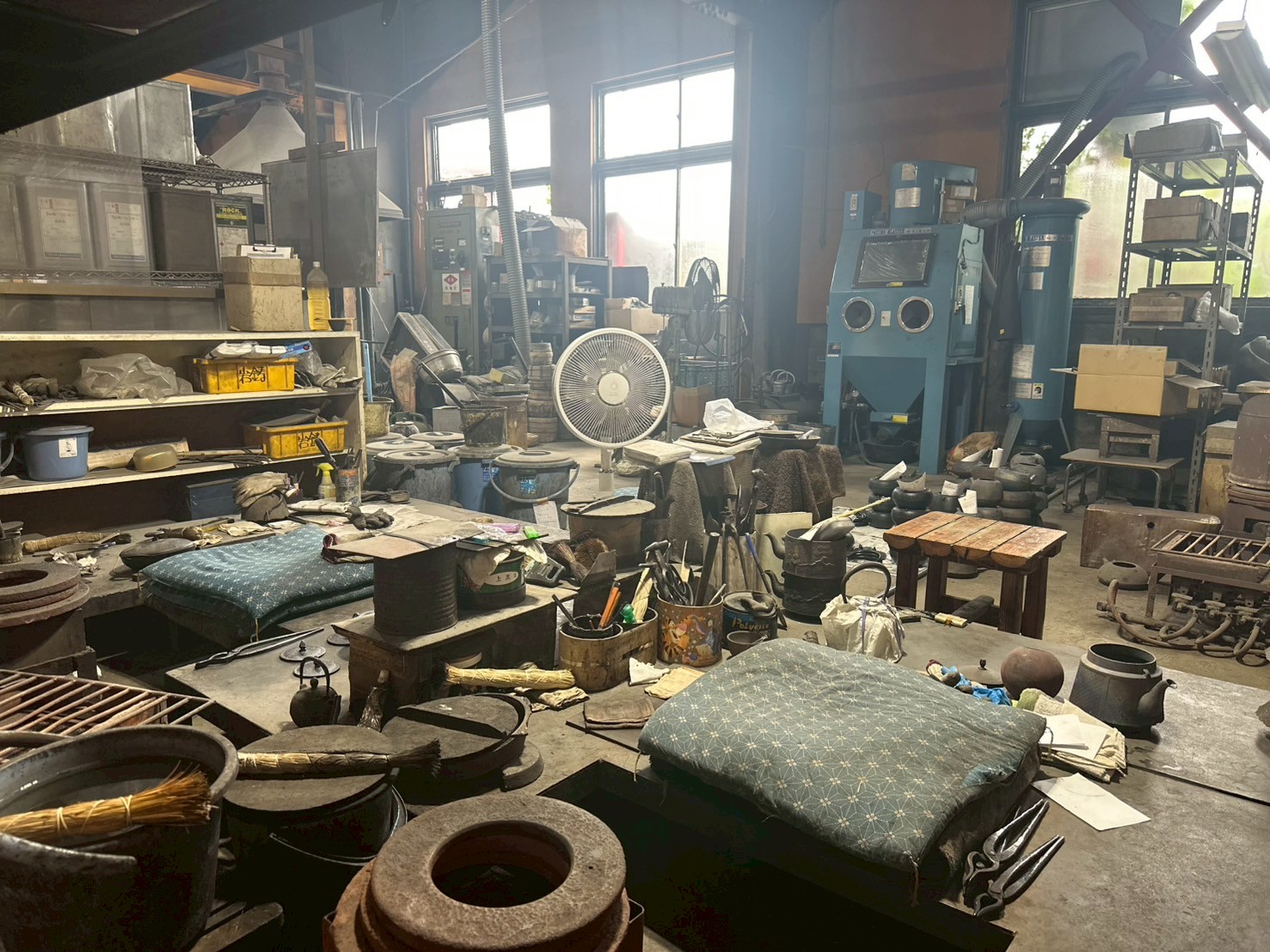 岩鋳工房の作業場、座布団の置かれた仕上げ台と道具、奥に砂型と排煙のフード
